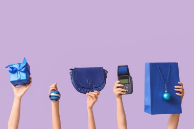 Alışveriş çantalı birçok kadın eli, Noel hediyesi kutusu ve mor arka planda ödeme terminali.