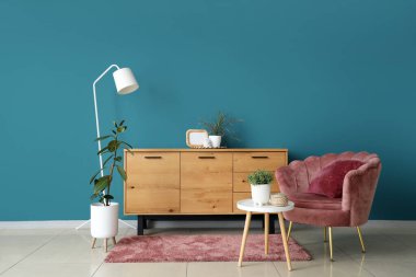 Rahat koltuğu, sehpası ve mavi duvarın yanındaki tuvaleti olan modern bir oda.