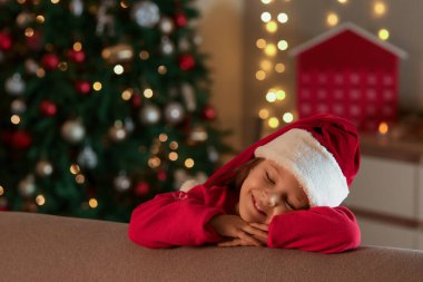 Noel Baba şapkalı şirin kız Noel arifesinde evde kanepenin yanında.