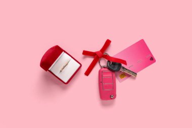 Yeni arabanın hediye anahtarları, kredi kartı ve pembe arka planda nişan yüzüğü.