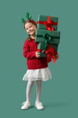 Geyik boynuzları takmış şirin küçük bir kız ve yeşil arka planda Noel hediyeleri.