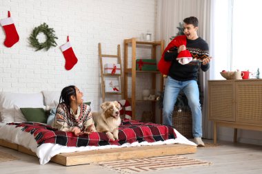 Noel arifesinde yatak odasında hediye dolu çantalı ve köpekli mutlu bir çift.