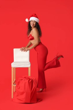 Güzel, genç, seksi, mutlu, Afro-Amerikan kadın. Kırmızı arka planda Noel Baba çantasıyla.