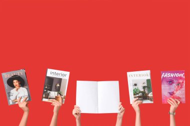 Kırmızı arka planda farklı dergileri olan kadın elleri