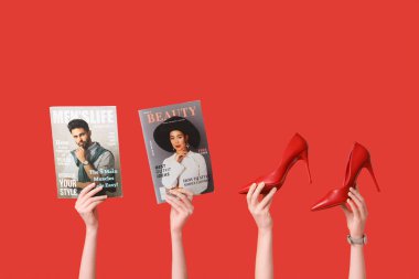 Farklı dergilere sahip kadın elleri ve kırmızı arka planda şık topuklu ayakkabılar.