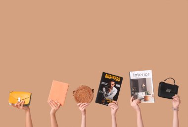 Farklı dergilere, kitaba ve kahverengi arka planda şık çantalara sahip kadın elleri.