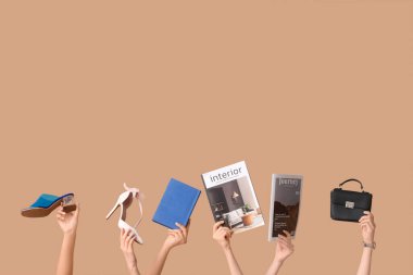 Dergi, kitap, topuklu ayakkabı ve kahverengi arka planda şık bir el çantası olan kadın elleri.