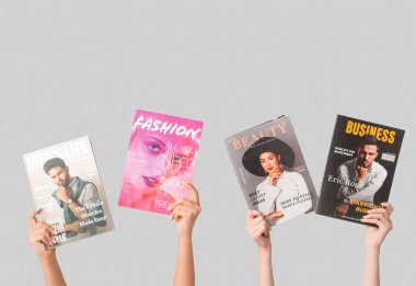 Gri arka planda farklı dergilere sahip kadın elleri