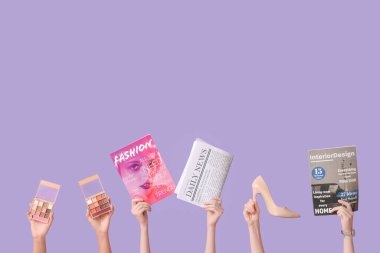 Farklı dergilere, gazetelere, yüksek topuklulara ve eflatun arkaplanına sahip kadın elleri.