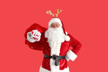 Noel Baba geyik boynuzlarıyla kırmızı arka planda Noel çantası ile