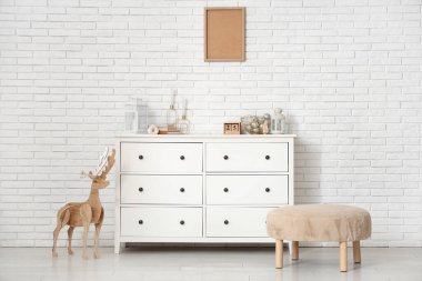 Tahta geyik, puf ve çekmeceler beyaz tuğla duvarın yanında.