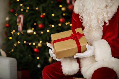Noel Baba elinde hediye kutusuyla evde Noel ağacının yanında, yakın plan.