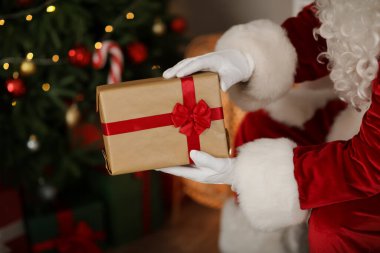 Noel Baba elinde hediye kutusuyla evde Noel ağacının yanında, yakın plan.