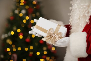 Noel Baba elinde hediye kutusuyla evde Noel ağacının yanında, yakın plan.