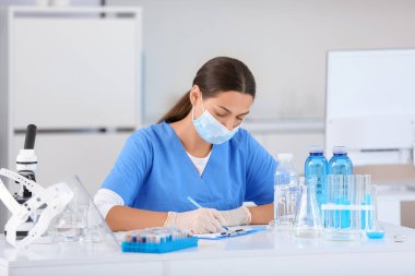 Profesyonel cam takımlı genç bir bilim adamı araştırma laboratuvarında su kalitesini ve yazı tahtasına yazmayı inceliyor.