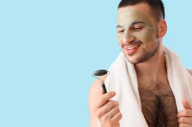 Yüzünde kozmetik jel maskesi ve mavi arka planda masaj maskesiyle yakışıklı genç bir adam.