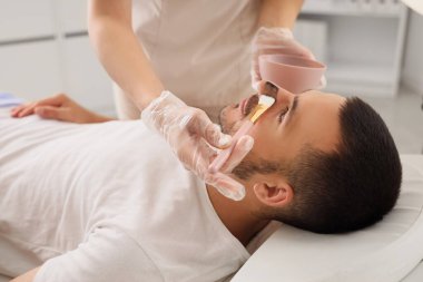 Güzellik uzmanı, güzellik salonunda yakışıklı adamın yüzüne kozmetik balon maskesi takıyor.