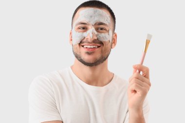 Yüzünde kozmetik balon maskesi ve gri arka planda fırçası olan yakışıklı genç adam.