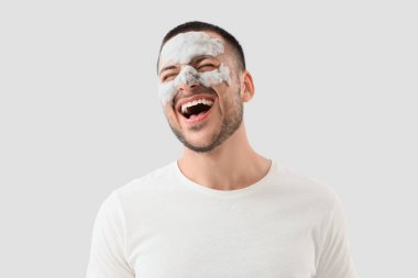 Yüzünde kozmetik balon maskesi olan yakışıklı genç adam gri arka plana gülüyor.