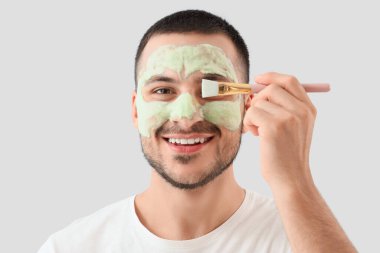 Yüzünde kozmetik balon maskesi ve gri arka planda fırçası olan yakışıklı genç adam.