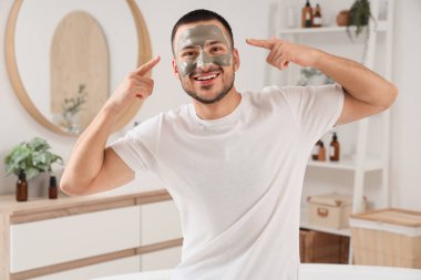 Yakışıklı genç adam banyodaki kozmetik kil maskeyi işaret ediyor.