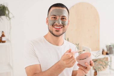 Evdeki banyoda yüzünde kozmetik kil maskesi olan yakışıklı genç adam.