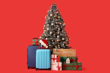 Güzel dekore edilmiş Noel ağacı hediye kutuları, bavullar ve kırmızı arka planda Merry Noelleri ile
