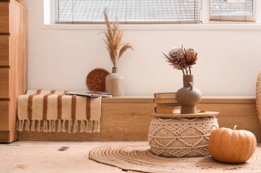 Çiçekli kahve masası, balkabağı ve oturma odasının sonbaharında beyaz duvarın yanında rahat bir bank.