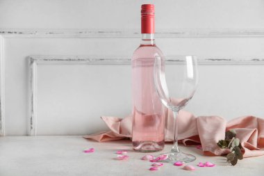 Cam, okaliptüs ve beyaz arka planda gül yapraklı bir şişe lezzetli pembe şarap.