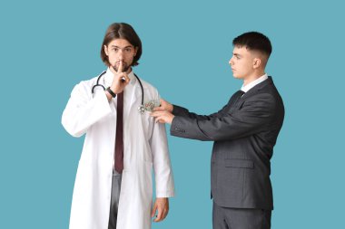 Young man putting bribe into doctor's pocket on blue background. Corruption concept clipart