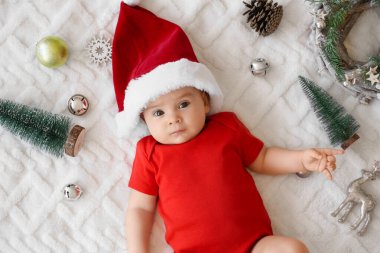 Noel Baba şapkalı, yumuşak bir battaniyeye uzanmış şirin bir bebek.