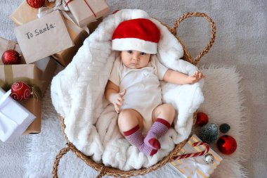 Noel Baba şapkası ve Noel süslemeleri olan şirin bir bebek evde sepette yatıyor.