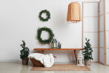 Oturma odasının içinde Noel ağaçları, çelenkler ve ahşap banklar var.