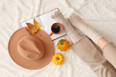 Balkabağı kahveli genç bir kadın, sonbahar yapraklı ve kitaplı yatakta oturuyor.