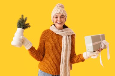 Sarı arka planda Noel dalları ve hediye kutusu olan genç bir kadın.