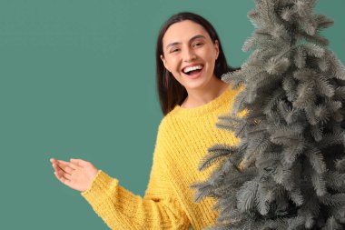 Yeşil arka planda Noel ağacı olan genç ve güzel bir kadın.