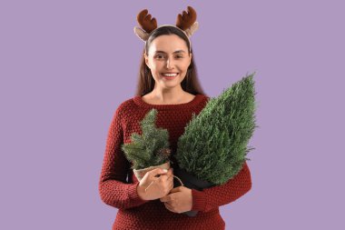 Geyik boynuzları takmış genç ve güzel bir kadın Noel ağacı ve mor arka planda saksıda dallar.