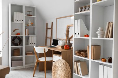 Sonbahar dekoru, işyeri ve raf üniteleriyle aydınlık oturma odasının içinde.