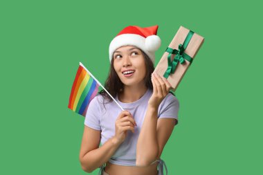 Noel Baba şapkalı genç Asyalı kadın LGBT bayrağı ve yeşil arka planda Noel hediyesiyle