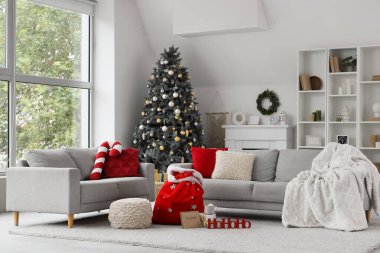 Oturma odasının içinde kanepeler, Noel ağacı ve Noel çantası var.