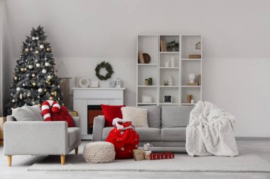 Oturma odasının içinde kanepeler, Noel ağacı ve Noel çantası var.