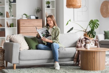Oturma odasındaki kanepede iç tasarım dergisi okuyan genç bir kadın.