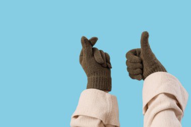 Sıcak eldivenli kadın mavi arka planda el kol hareketi yapıyor.