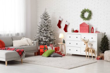 İçinde gri kanepe, Noel ağacı ve hediye kutuları olan şenlikli bir oturma odası.