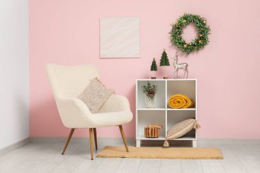 Koltuğu, raf ünitesi ve pembe duvarında Noel çelengi olan modern bir oda.