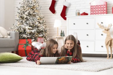 Evde kitap okuyan, damalı pijamalı şirin mutlu kızlar.