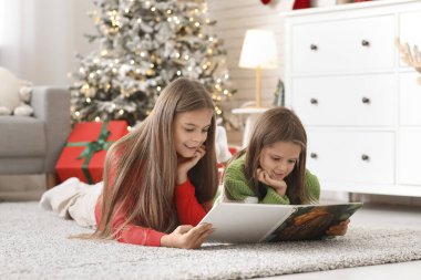 Evde kitap okuyan sevimli mutlu küçük kızlar.