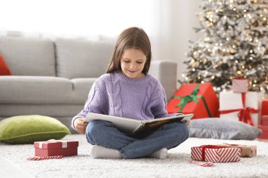 Evde kitap ve hediye kutularıyla Noel hikâyesi okuyan sevimli, mutlu küçük bir kız.