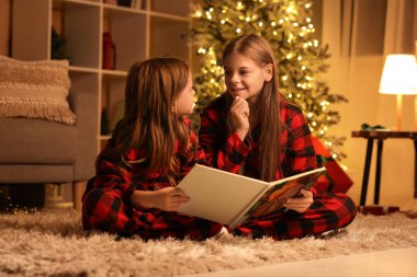 Kareli pijama giymiş, geceleri kitap okuyan sevimli mutlu küçük kızlar.