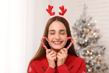 Noel arifesinde evde geyik boynuzlarıyla şeker kamışı taşıyan genç bir kadın, yakın plan.